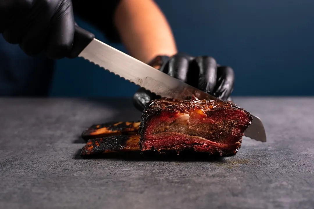 Brisket being sliced with a black-gloved hand